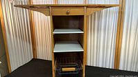 Front view of wooden kitchen island cart with both drop leaf sides extended showing drawer, two white shelves, and metal wire basket on wheels.