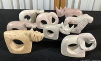 Full set of eight carved stone animal napkin rings arranged on black background showing variety of animals including rhino, elephant, lion, and hippo in varying light stone colors