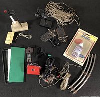 Photo showing all items in the lot arranged on a black surface: two signal lights, assorted switches, wiring, connectors, smoke fluid in original packaging, and a curved track piece.
