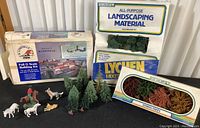 Overall image showing assorted model train landscaping items including boxed trees, lychen, miniature figures, and building kits.