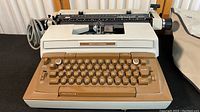 Front-facing photo of the vintage Smith Corona Coronamatic 8000 electric typewriter on a dark surface, showing beige and brown keys and metal accents with power cord visible.