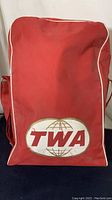 Front view of red vinyl bag showing TWA logo and wear on material.
