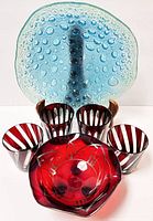 Blue blown bubble art glass plate displayed on wooden stand with ruby red bowl and four juice glasses in front.