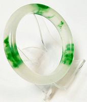Photo of jade bangle bracelet on clear stand showing green veins and translucency.