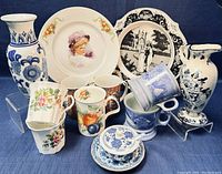 Wide shot showing the full assortment of chinaware including plates, mugs, mugs stacked, and two vases at either side.