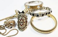 Close-up photo showing the chain necklace, three stretch bracelets (gold-tone ribbed, silver-tone with black rhinestones, and gold-tone with black enamel), and two rings including an elongated red rhinestone ring and an animal-shaped rhinestone ring.