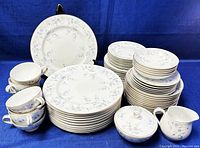 Full set of Mikasa Winston china including stacked plates, bowls, teacups, sugar bowl, and creamer against blue background.