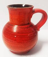 Red-orange round pottery jug with handle and minor rim chips, glossy finish with dark interior glaze.