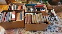 Wide view of three boxes filled with hardcover books of various sizes and colors, some vintage, some modern.