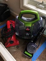 Full view of the Bissell Little Green ProHeat Pet carpet cleaner alongside the Dirt Devil handheld vacuum, showing the design, handle, and attachments.