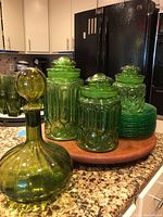 Photo showing decanter, canisters, wooden Lazy Susan, and stacked green plates