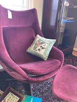Front view of burgundy velour swivel chair showing curved seat and backrest with decorative pillow