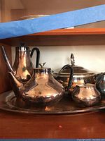 Image showing tea pot, coffee pot, sugar bowl, creamer, covered casserole dish, and serving tray arranged on shelf.
