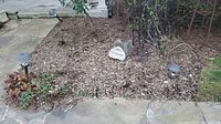 Overview showing two used solar yard lights staking mulch bed with welcome rock and boot scraper behind