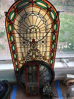 Tall arched stained glass panel leaning against window with smaller pieces in front