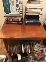 Top of the teak side table with visible wear and stacks of books and CDs on surface and below.