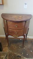 Front view of the half-moon wooden table showing two drawers, brass ring handles, floral inlay on the top surface, and brass decorative features