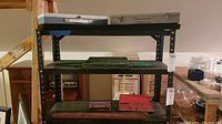 Three shelves shown with two silver metal boxes on top, wooden and black cases on the middle and lower shelves