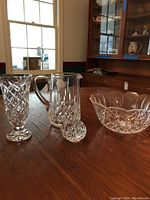 Full view of all four items including the tall vase, water pitcher, serving bowl and egg paperweight on table with wooden background.