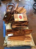 Overview of multiple wooden kitchen utensils including spoons, rolling pins, cutting boards, cedar planks, a Lazy Susan, and a serving tray placed on a table.