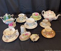 Wide shot of antique china set including teapot, creamer, sugar bowl, multiple teacups and saucers with floral designs, small decorative plates, salt shaker, and mini bowl with spoon.