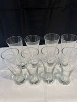 Eight beer glasses on a white cloth and a black background, showing two types of beer glasses with four each.