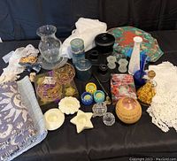 Wide view of assortment on black backdrop showing candles, candlestick holders, vases, white tablecloth, curtain ties and decorative small items