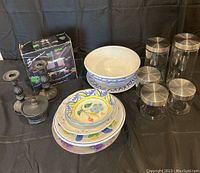 Overview photo showing five glass canisters with metal lids, large ceramic bowls/platter with blue designs, multiple colorful plates, a complete fondue set in original box, and two dark metal candlestick holders.