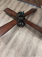 Top view of the ceiling fan showing four wide brown wooden blades and the central motor housing