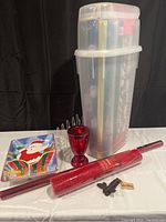 Clear plastic gift wrap organizer with wrapping materials, red glass candle holder, ceramic platter and door knocker on display.