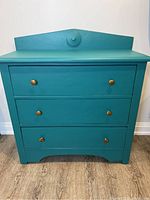 Front view of rustic teal dresser showing three drawers and bronze knobs