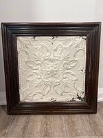 Framed antique tin ceiling tile from church ceiling, showing entire piece and wood frame.