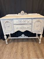 Front view of vintage painted buffet in antique white with ornate carved detailing and drawers and cabinets.