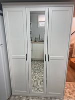 Front view of closed wardrobe showing three doors and full-length center mirror