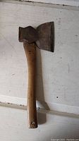 Hatchet laid flat showing the full wooden handle and large metal head with some rust and wear.