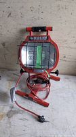 Red Husky utility work light with protective metal cage over bulb, bundled power cord with plug, placed on a work surface.