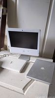 Three devices displayed: white iMac upright at back, closed white plastic MacBook and closed silver aluminum laptop in front