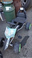 Single kids pedal race car with black seat, metal frame, green wheels, and worn racing graphic panel on front.