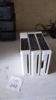 Three white Nintendo Wii consoles standing vertically, showing front disc slots and top controller ports.