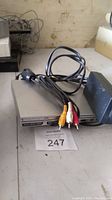 Silver Sony PlayStation 2 slim console with power AC adapter and composite AV cables on a surface