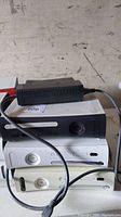Three Xbox 360 consoles stacked, one black faceplate and two white consoles, with one power cable laid on top