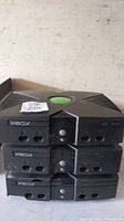 Stacked three original black Xbox consoles with visible wear and dust, no controllers or cables shown.