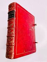 Red leather bound cover with gilt decoration, raised bands and two metal clasps