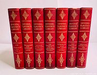 Photo of the seven leather bound book spines with gold embossed titles from the Universal Classics Library series in red covers.