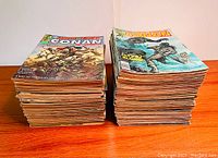 Two stacks of Conan magazines displayed on wooden table against plain background