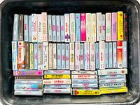Top-down view showing cassette tapes stacked in trays with visible artist names and album titles from the 1990s.