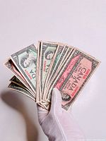 Hand holding a fanned assortment of old Canadian $1 and $2 bills showing design and circulation wear.