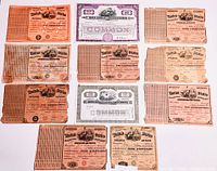 Photo showing all 11 vintage stock certificates laid flat, displaying attached coupons and various degrees of wear including discoloration and tears.