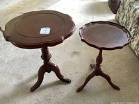 Two wooden side tables with scalloped edges and tripod bases placed on carpet, larger on left and smaller on right.