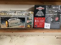 Two boxed Motomaster air compressors on wooden shelf. The box of the multi-purpose compressor is worn and damaged; the programmable direct drive compressor box is intact with product image and specifications.